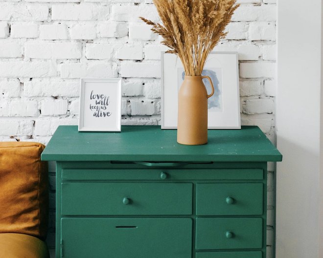 decorating furniture consisting of a dark green desk of with many drawers over which a vase of flowers and a small portrait